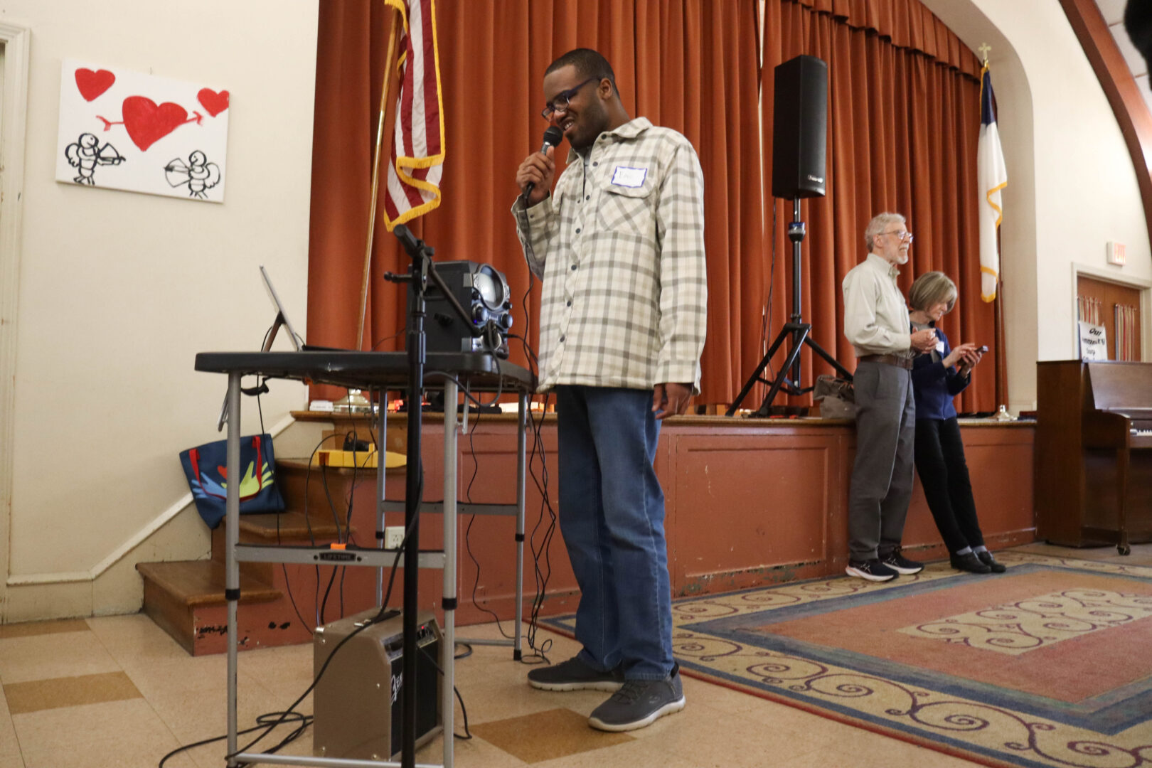 A man in a plaid shirt singing into a microphone on a stage at a community event.
