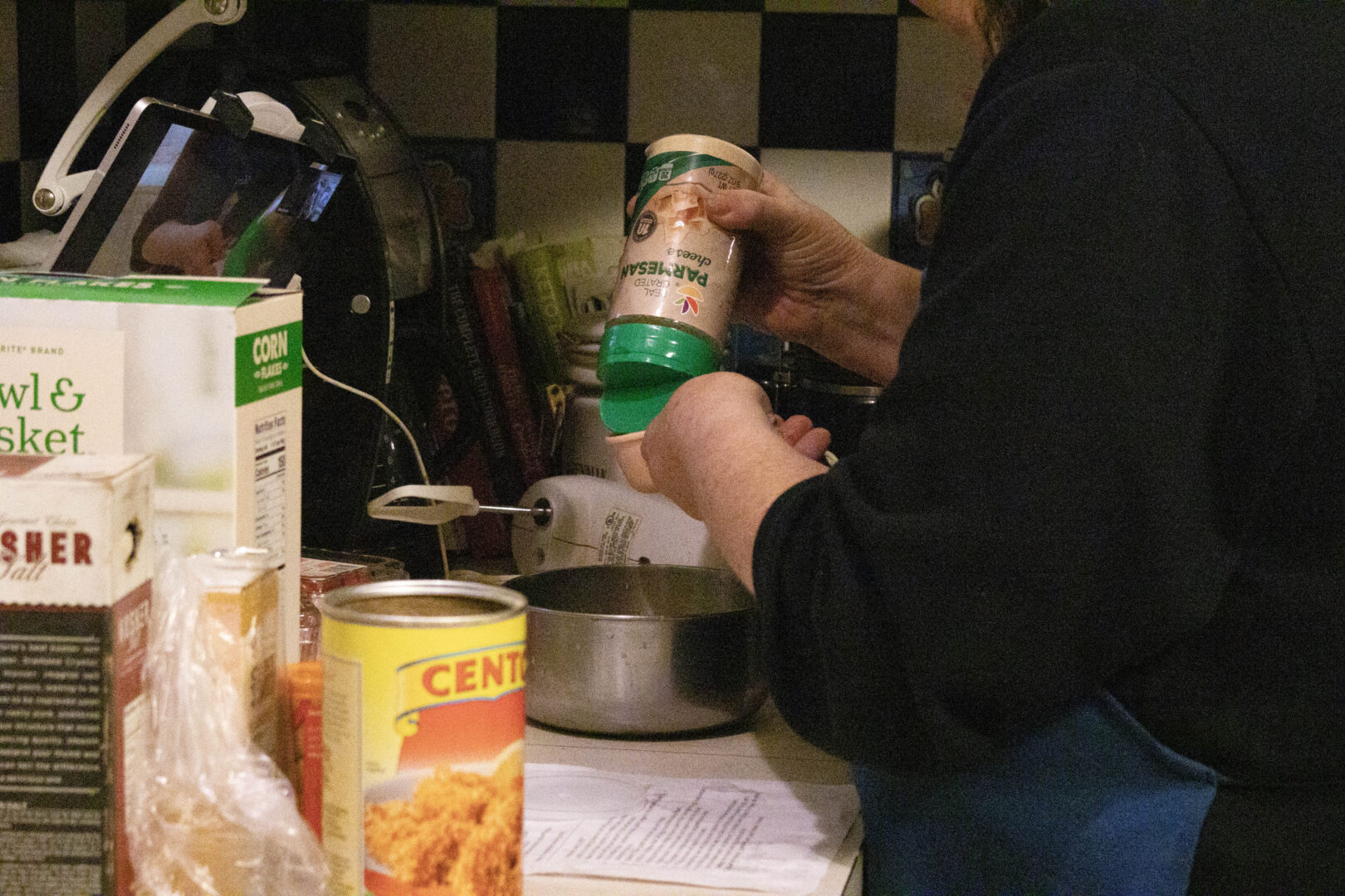 A close-up of a person pouring grated parmesan cheese into a measuring cup in a kitchen.
