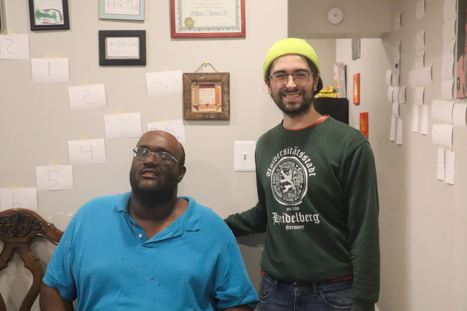 Two men, William and Noah, posing for a photo in a kitchen with notes pinned to the wall.